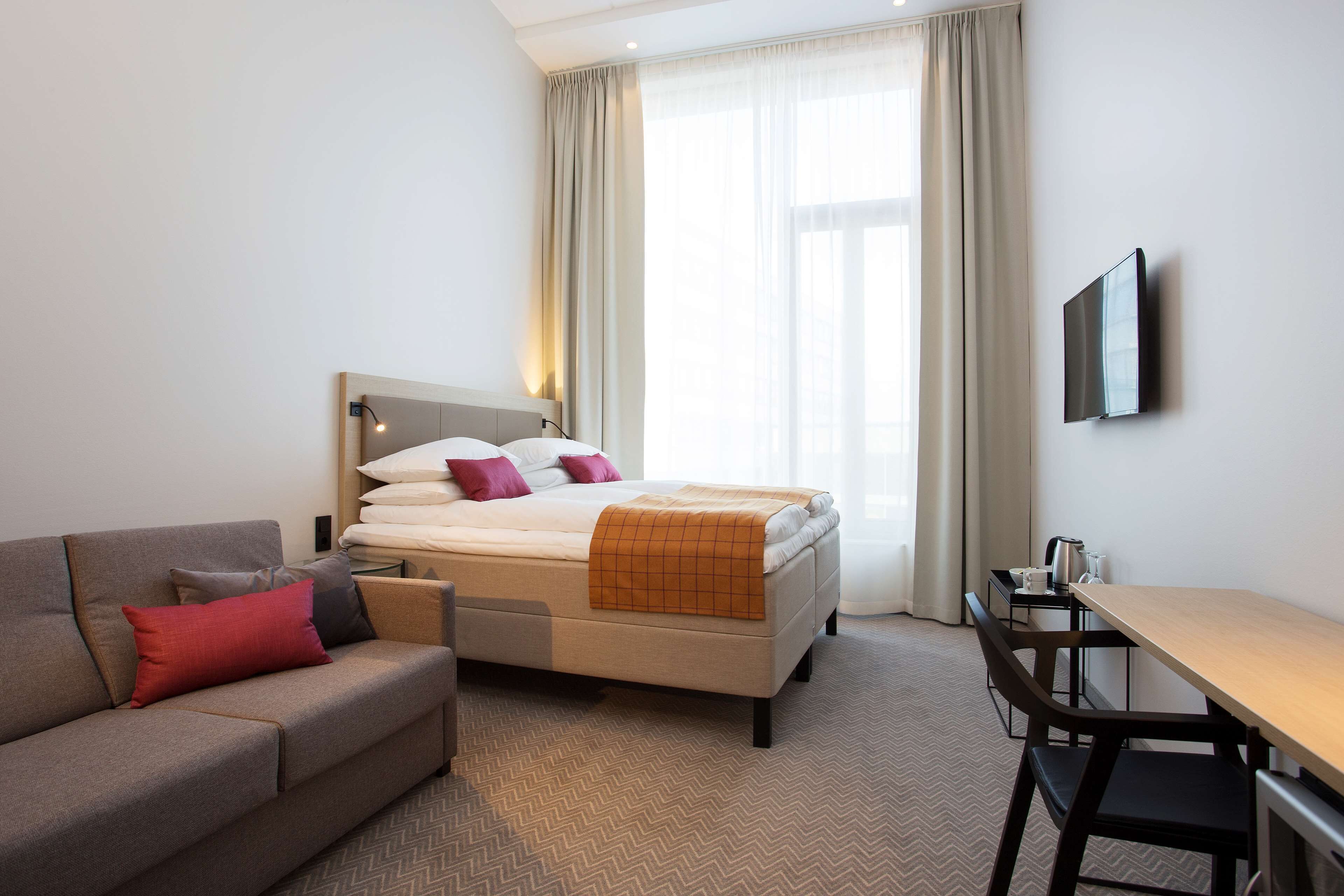 A hotel room with a bed, a sofa, a desk, and a TV.