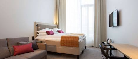 A hotel room with a bed, a sofa, a desk, and a TV.
