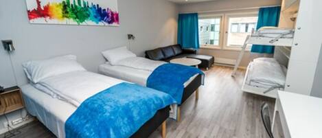 Habitación de hotel con dos camas, un escritorio, una silla, un ventanal con cortinas y una obra de arte de colores en la pared.