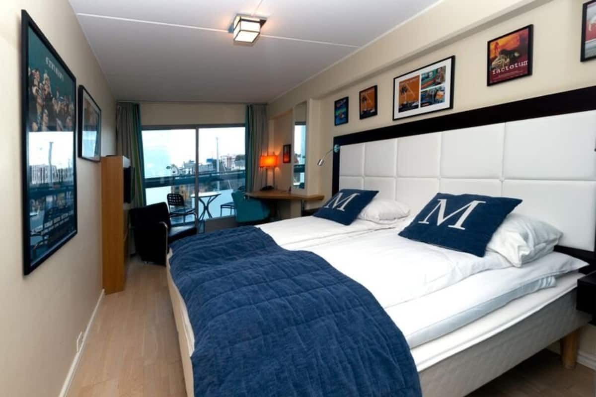 Hotellihuone, jossa on suuri sänky, työpöytä ja näkymä kaupunkiin.