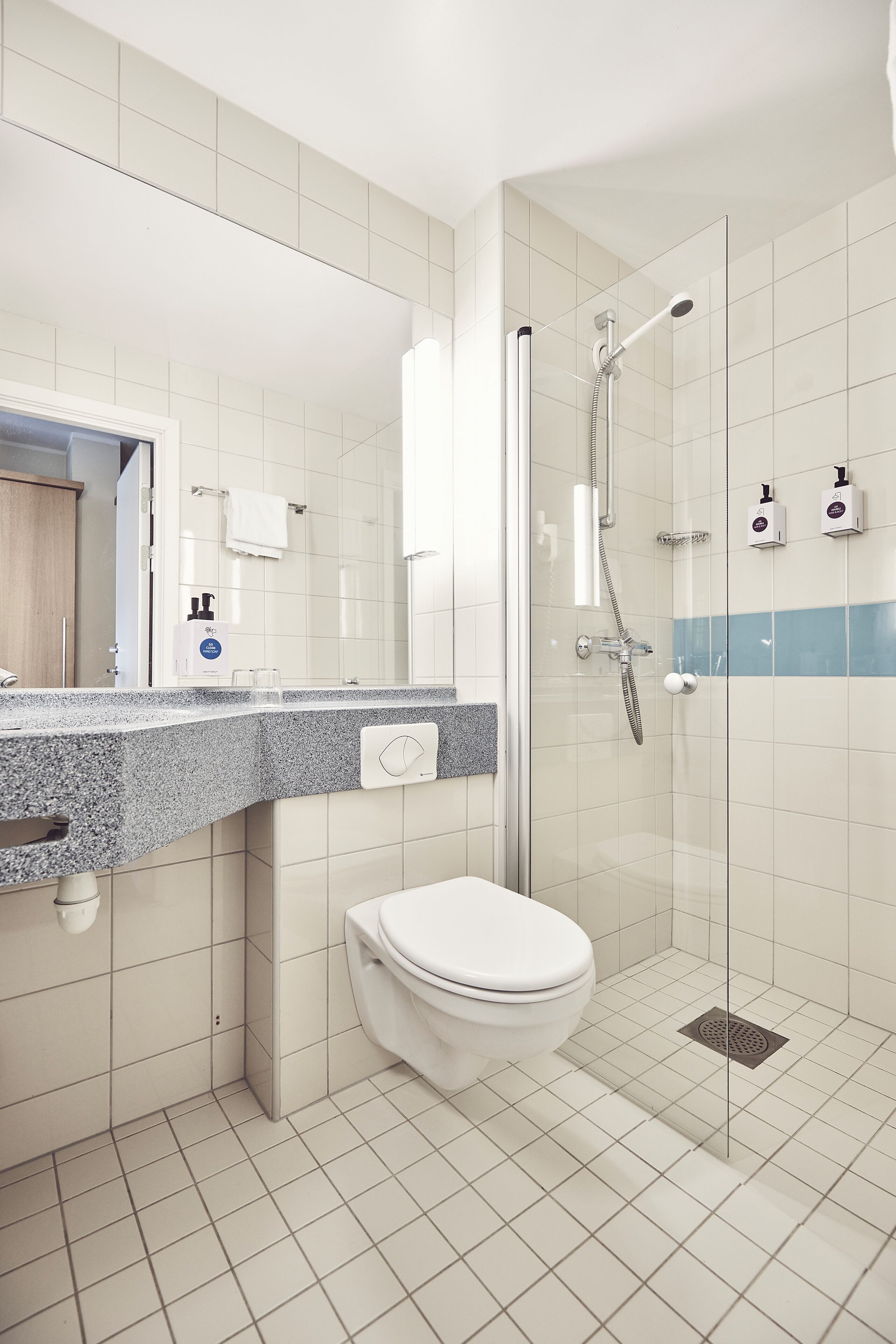 Une salle de bain moderne avec une douche à parois de verre, des toilettes blanches et un comptoir en granit doté d’un distributeur de savon.