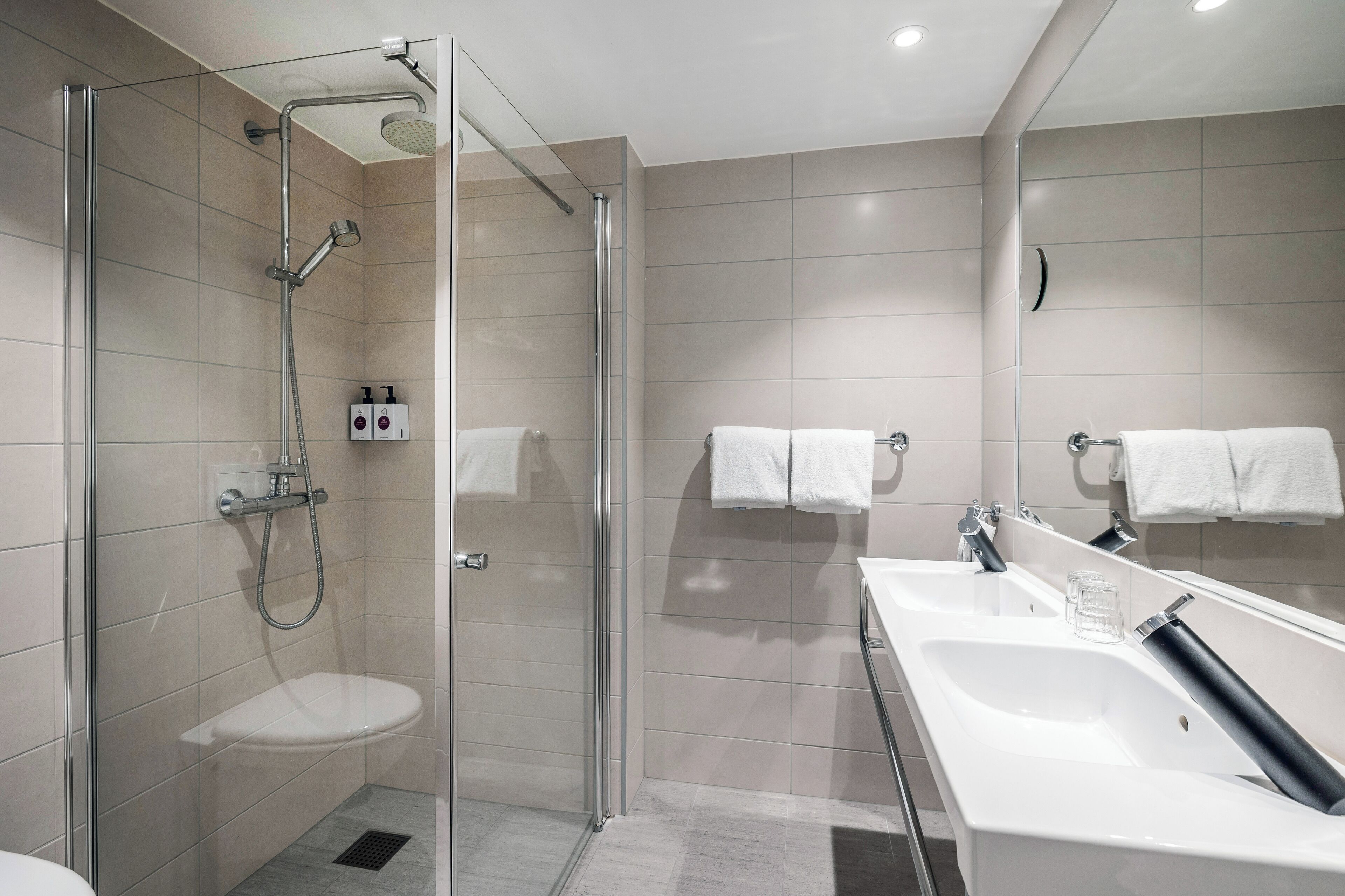 Un baño moderno con ducha envuelta en vidrio, un lavamanos blanco y un espejo grande.