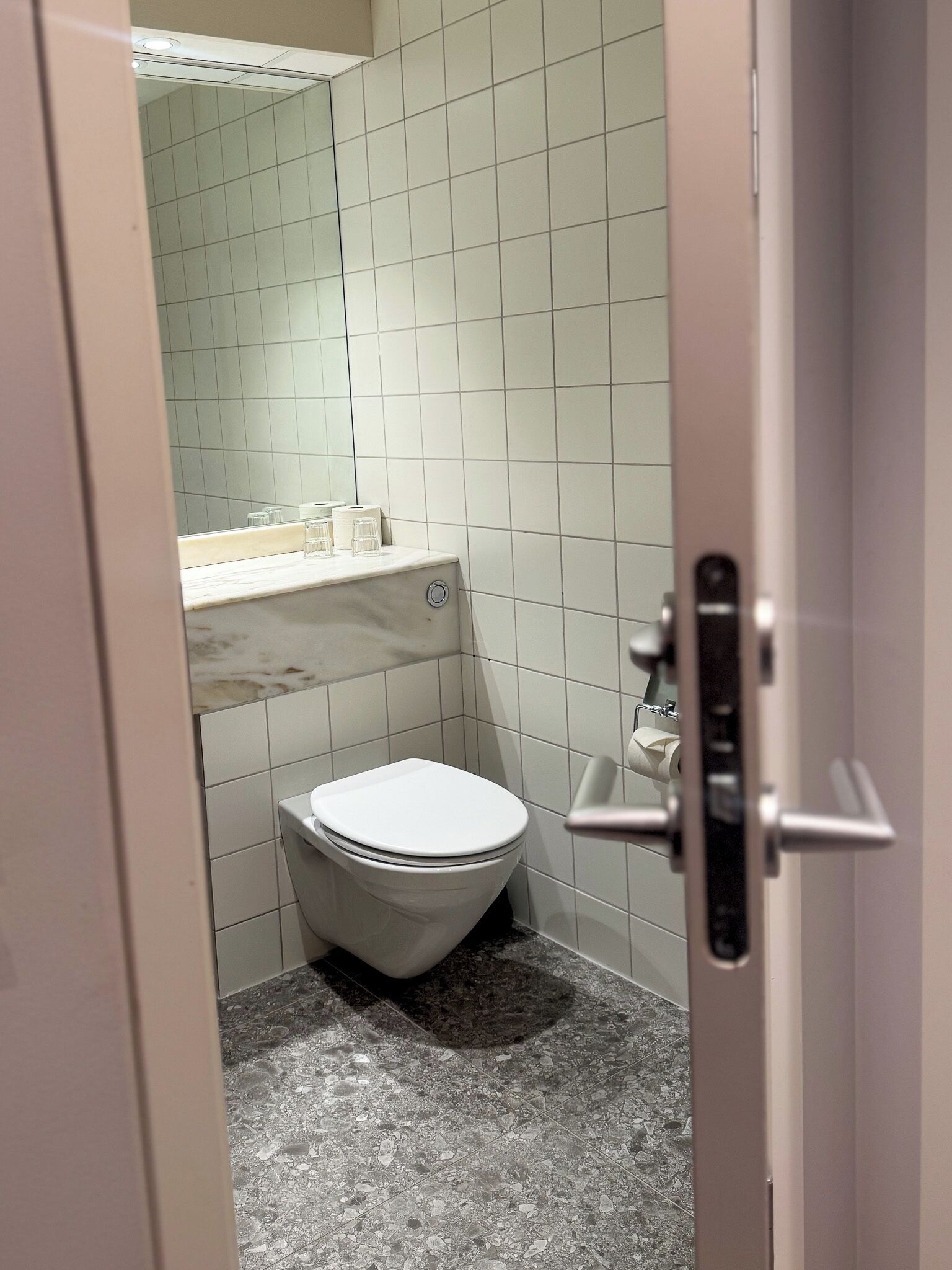 A small, modern bathroom with a toilet, a sink with a mirror, and a tiled floor.