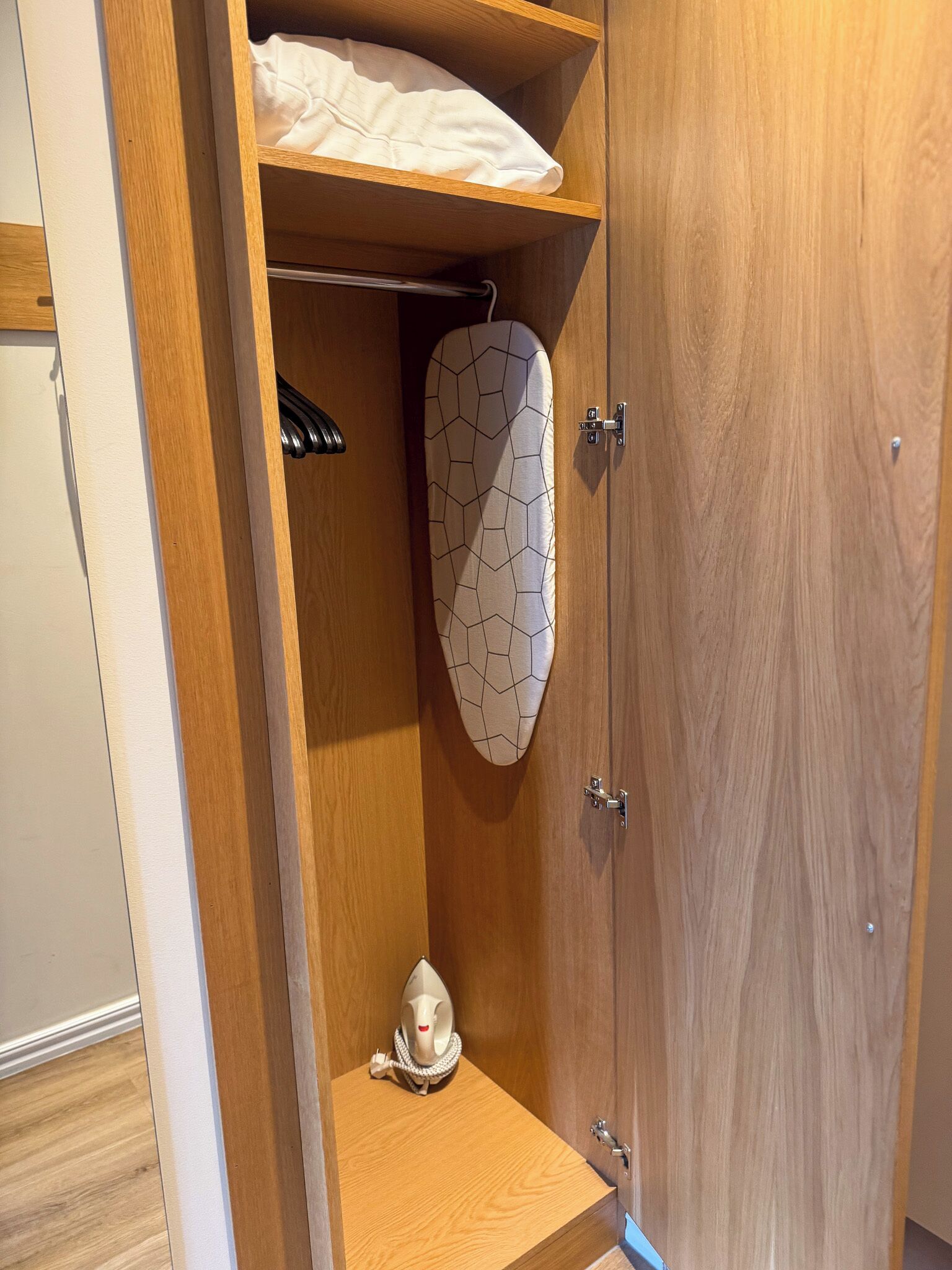 Un armario de madera con un plancha colgada y un objeto decorativo en el estante inferior.