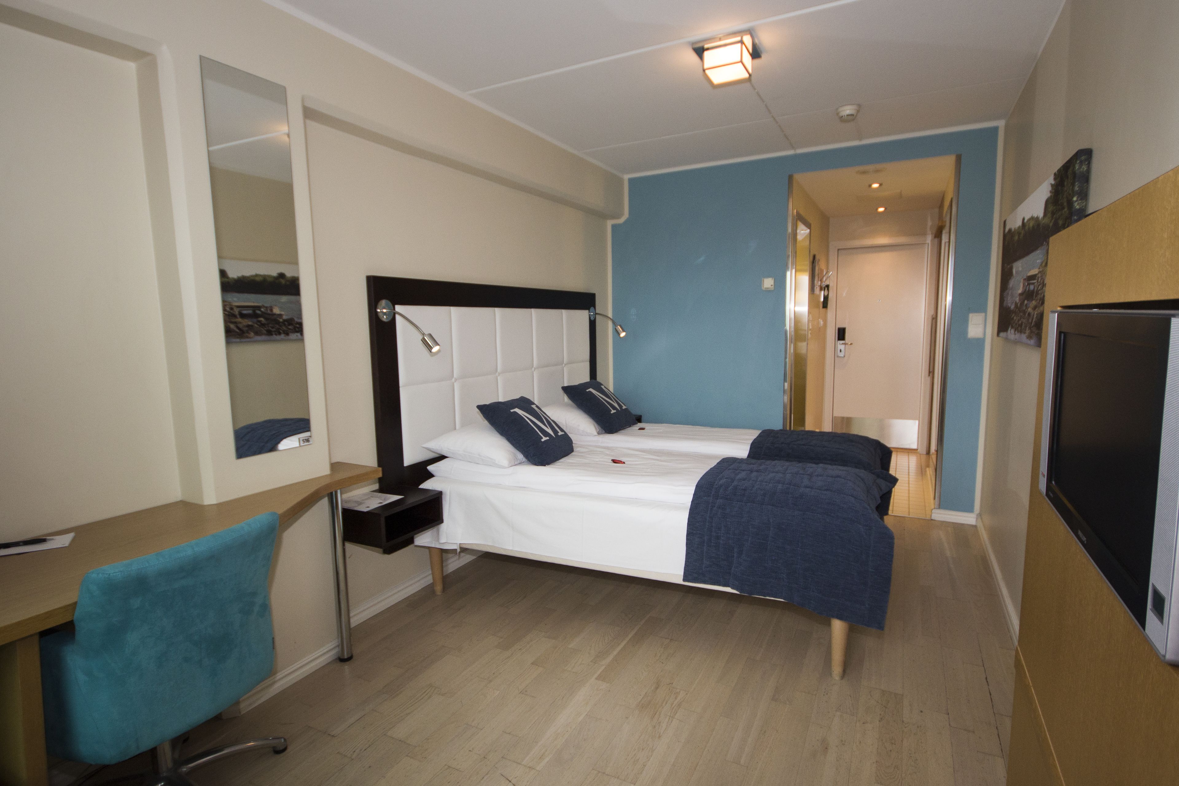 A hotel room with a bed, a desk, a chair, a TV, and a mirror.