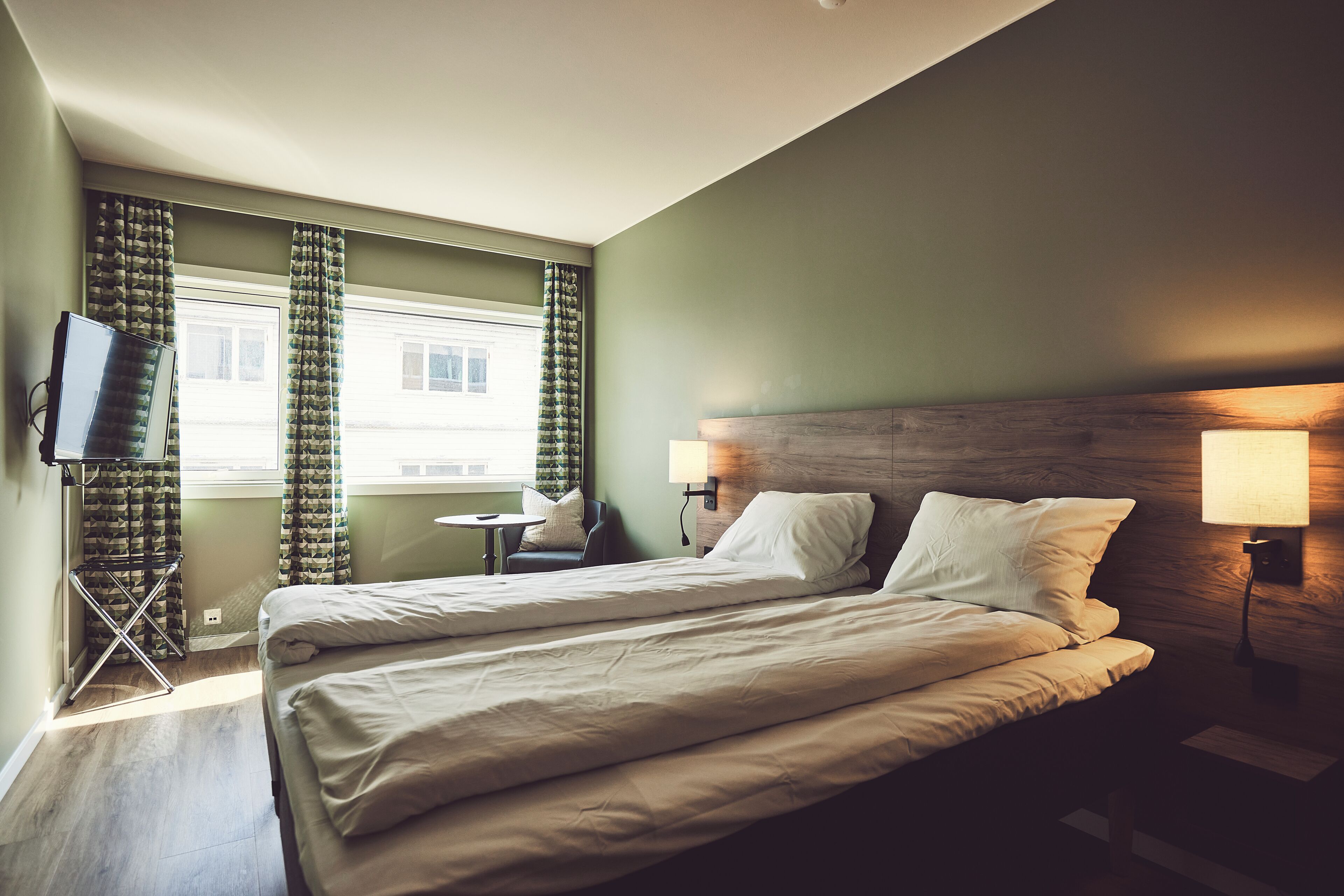 A hotel room with two beds, a TV, a small table, and curtains.