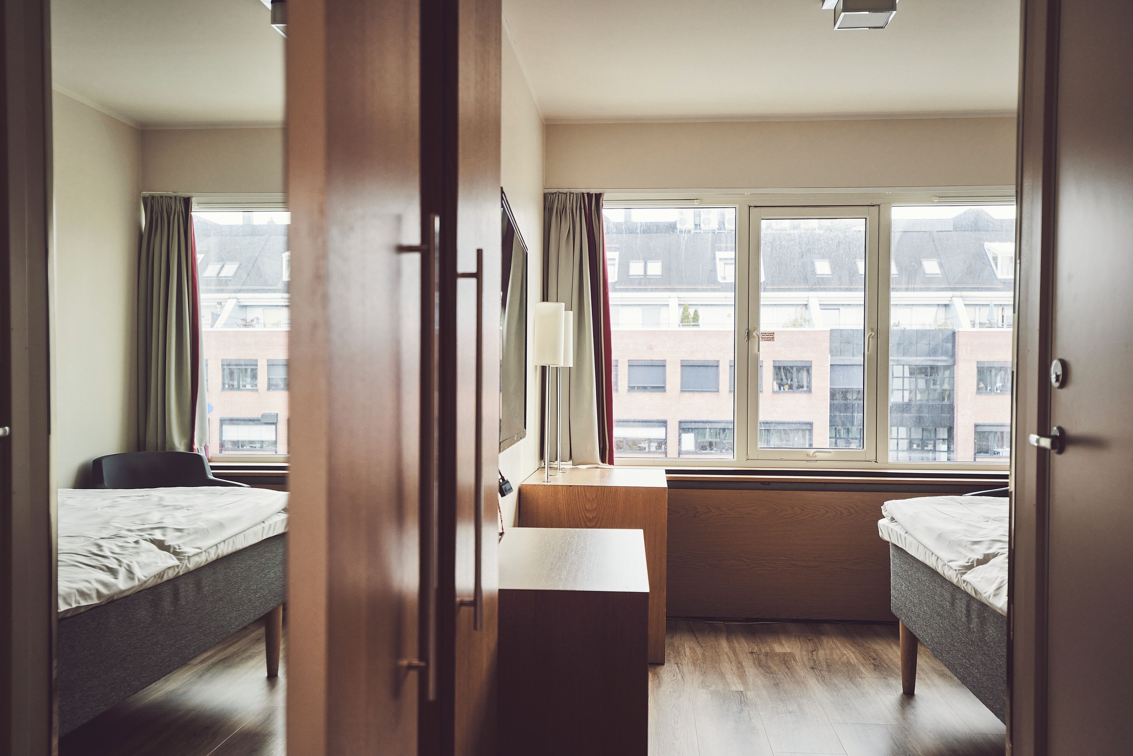 Quarto de hotel com duas camas, uma mesa de trabalho e uma janela com vista para edifícios.