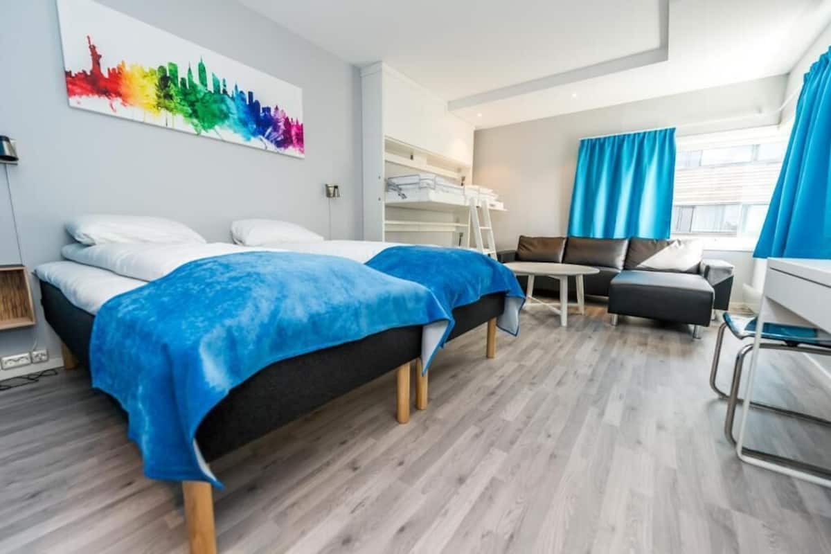 Moderni hotellihuone, jossa on kaksi sänkyä, sohva, työpöytä ja kerrossänky.