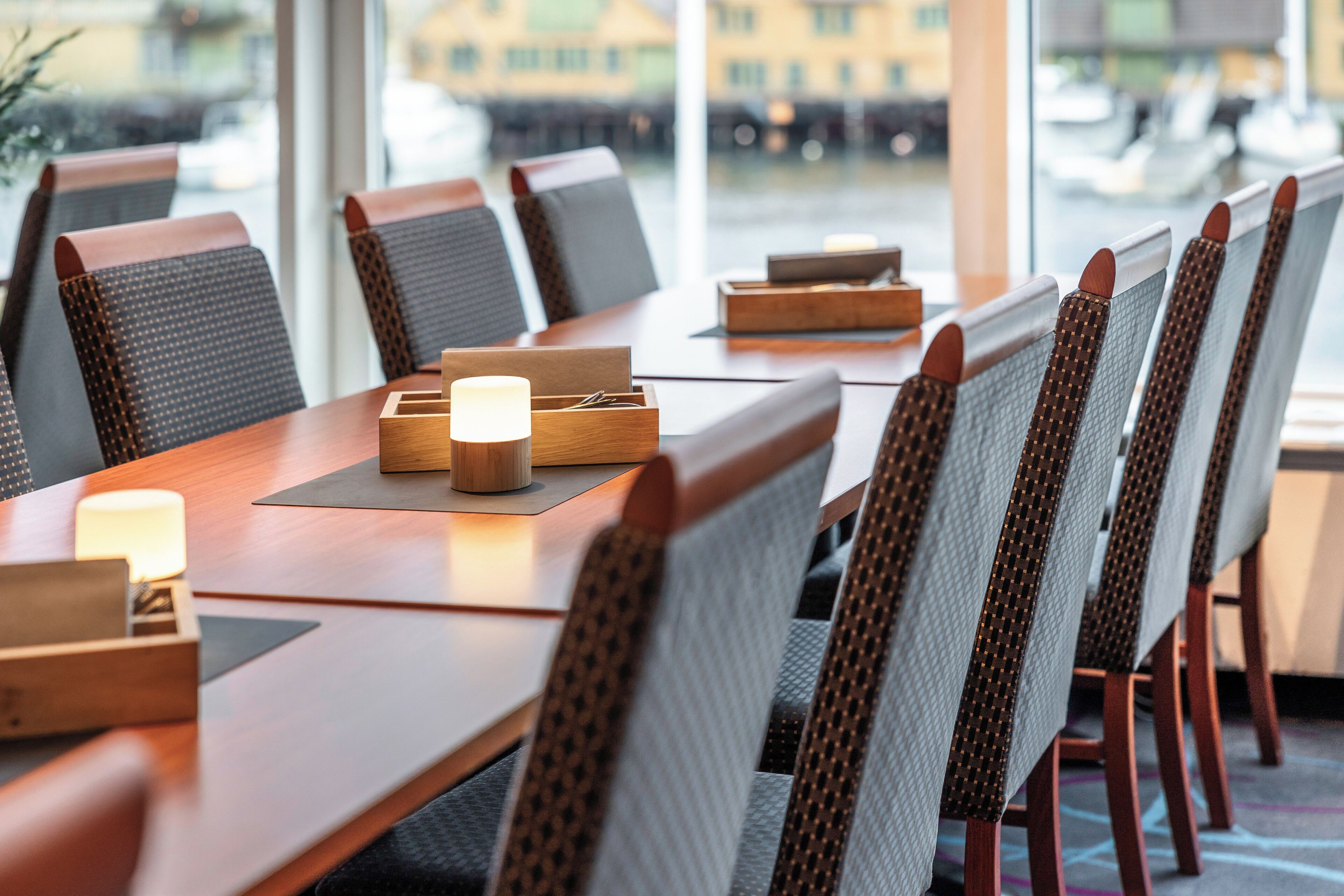 A dining area with a long wooden table, cushioned chairs, and candles.