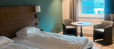 A hotel room with a large bed, two chairs, a small table, and a window with curtains.
