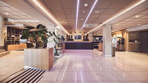 A modern hotel lobby with a reception desk, seating area, and a large plant.