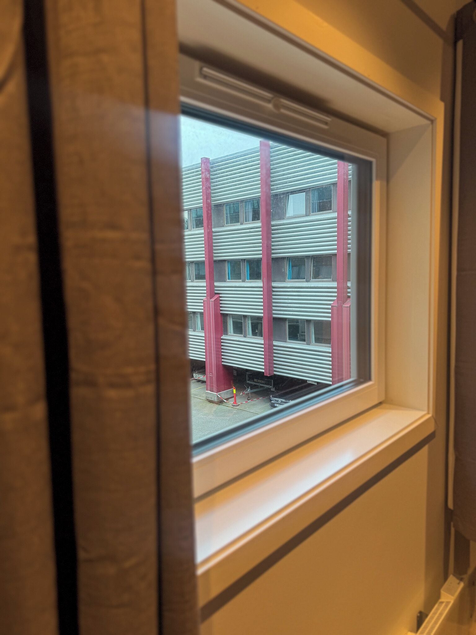Una ventana con vistas a un edificio de varios pisos y columnas rojas.