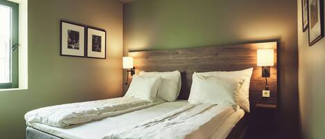Cama doble con ropa de cama blanca, dos lámparas de noche y dos cuadros en la pared.