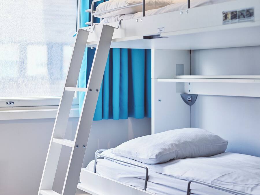 A bunk bed with a ladder, a window with blue curtains, and a white wall.