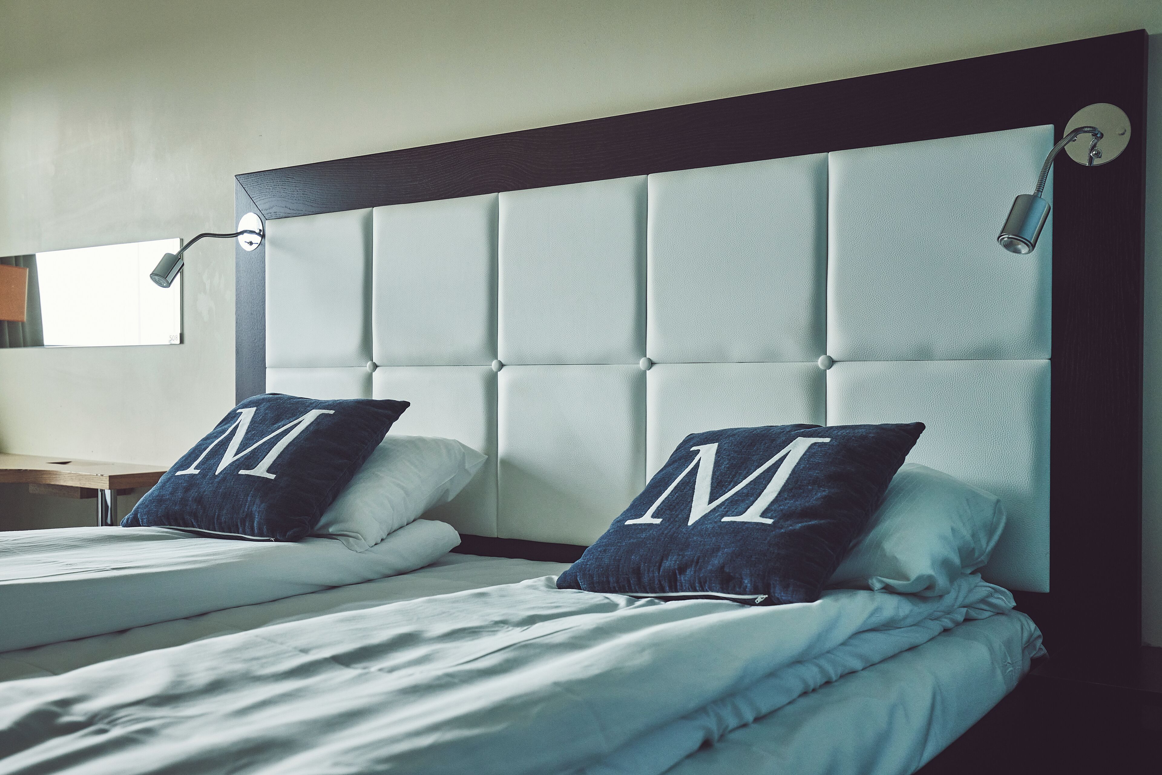 A hotel room with two beds, each with a pillow featuring a large 'M'.