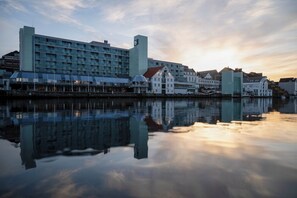Un hotel frente al agua, con un edificio moderno y casas tradicionales a lo largo de la orilla.