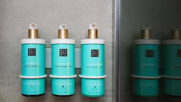 Tres botellas de productos 'Ritual de Karma': champú, gel de ducha y acondicionador, dispuestas sobre una pared de azulejos.