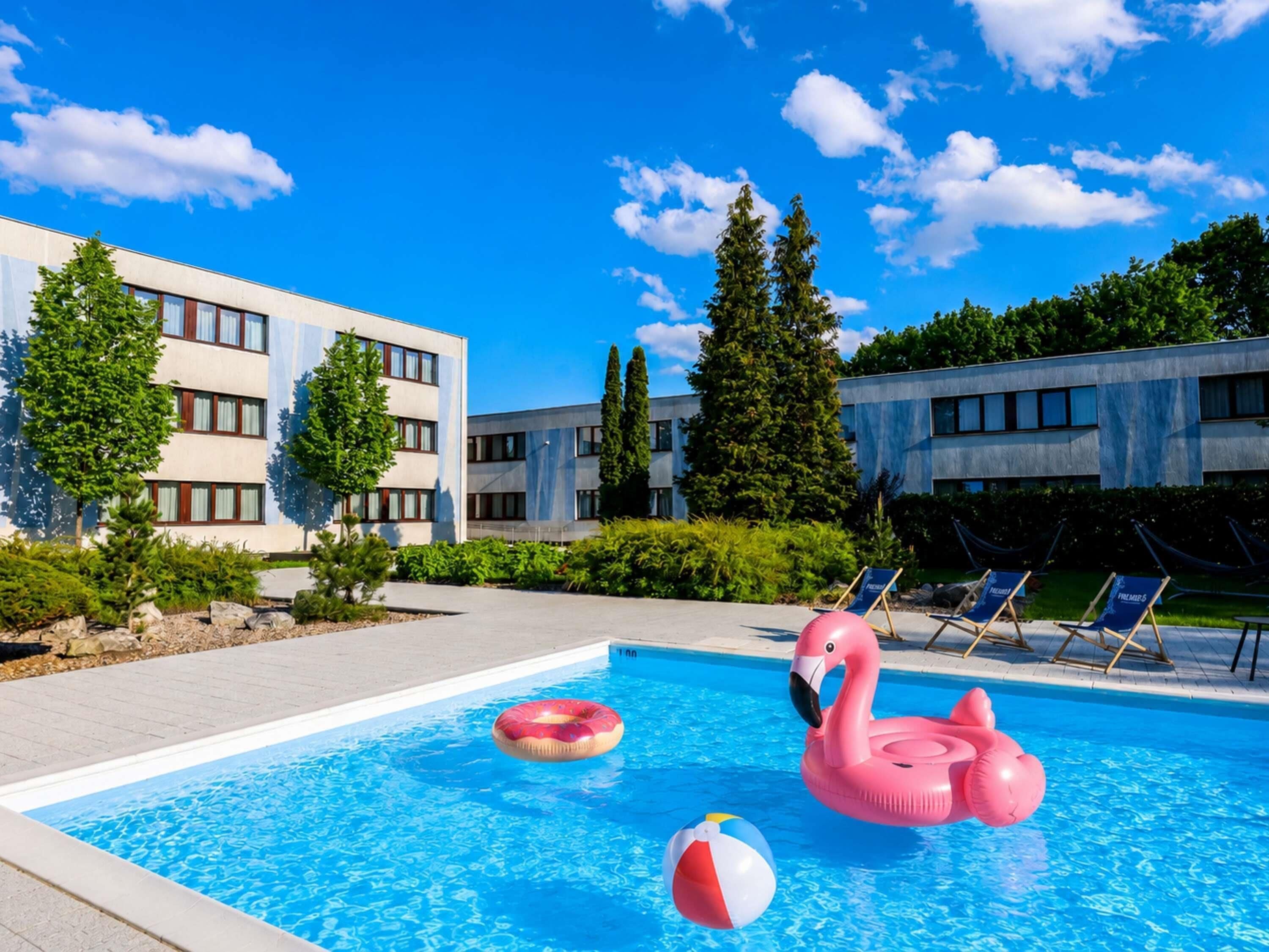 A swimming pool with inflatable toys, a lounge area with chairs, and modern buildings in the background.