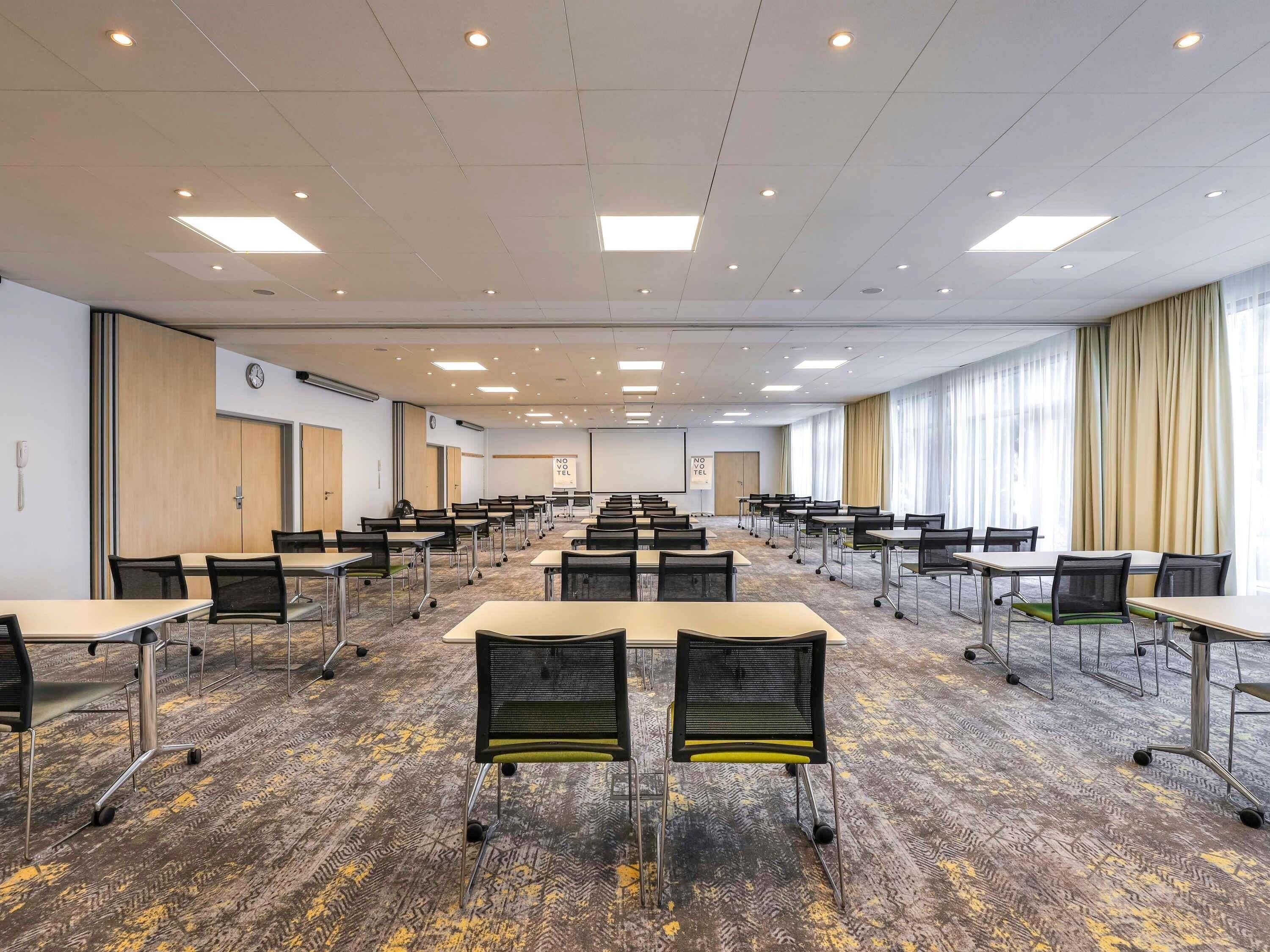 A conference room with multiple tables and chairs, a clock on the wall, and a large window with curtains.
