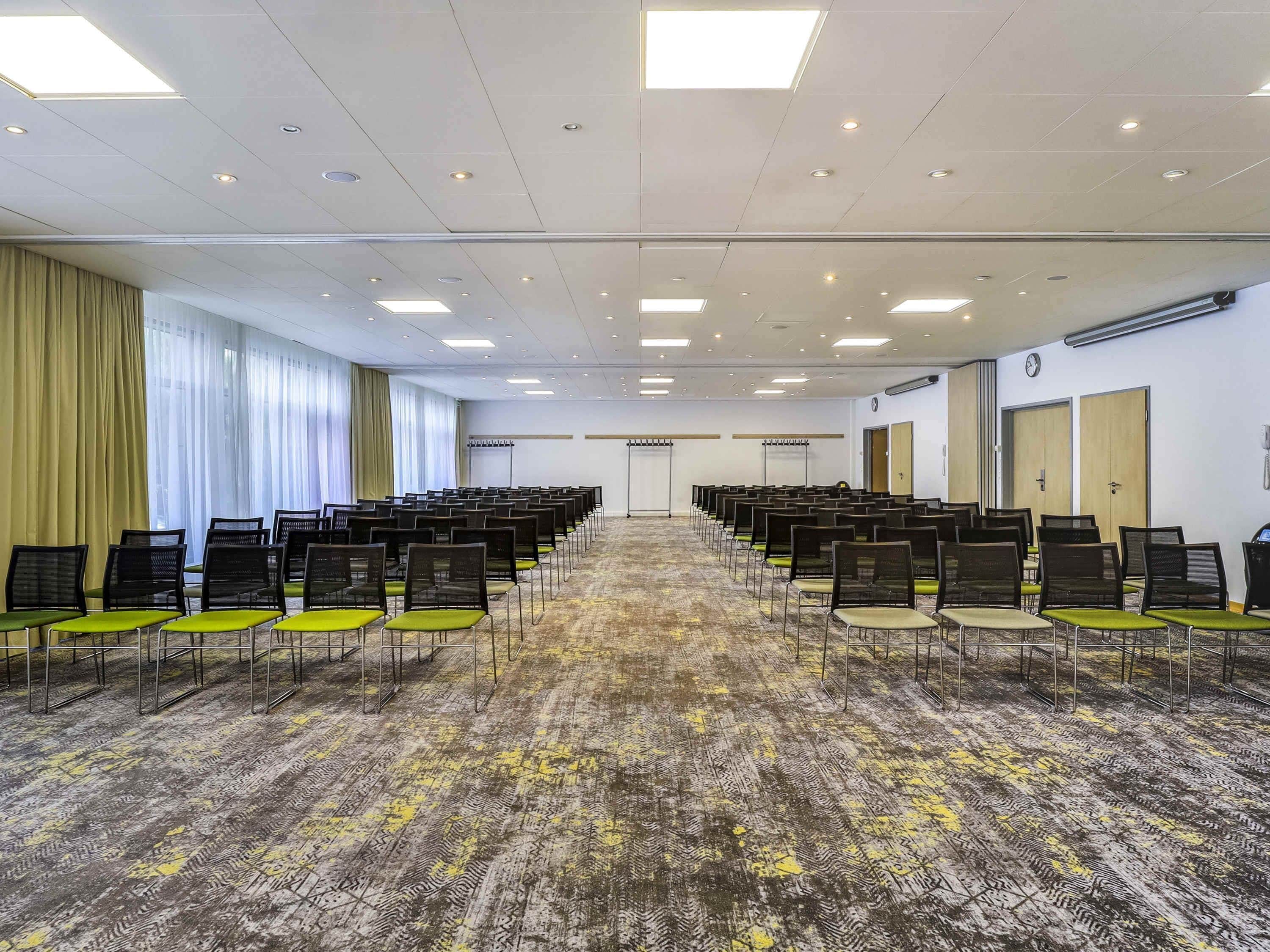 A conference room with rows of chairs, a carpeted floor, and a large window with curtains.