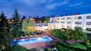 A hotel courtyard with a swimming pool, lounge chairs, and a well-maintained garden.