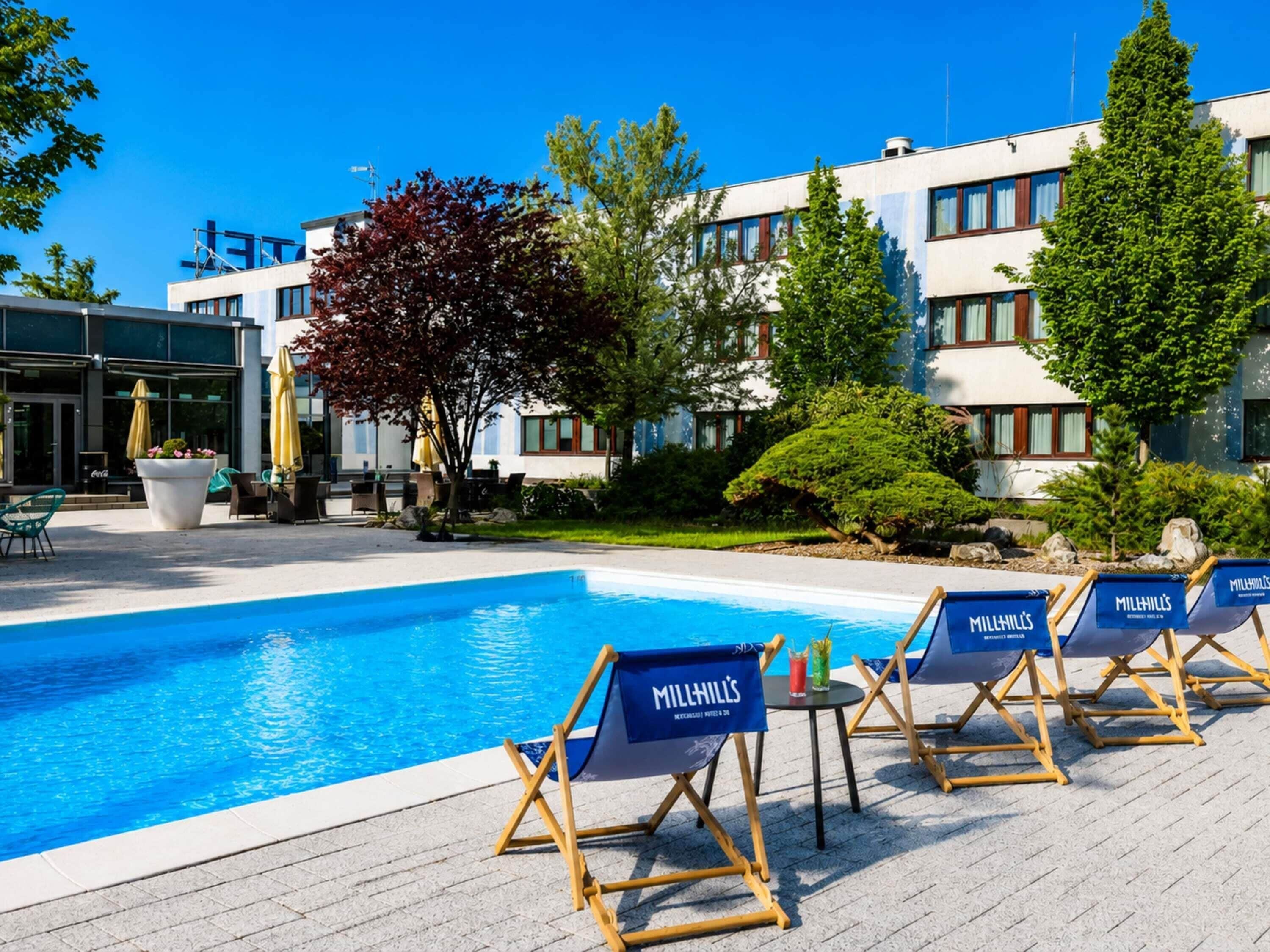Una piscina con sillas de descanso, una mesa y un edificio de diseño moderno al fondo.