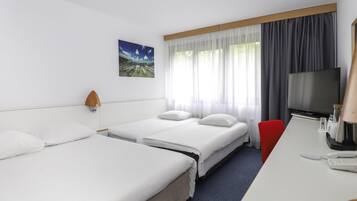 A hotel room with two single beds, a desk with a telephone, a television, and a window with curtains.