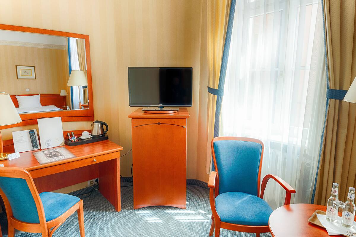 Ein Hotelzimmer mit Schreibtisch aus Holz, einem Fernseher, einem blauen Stuhl und einem kleinen Tisch mit Flaschen.