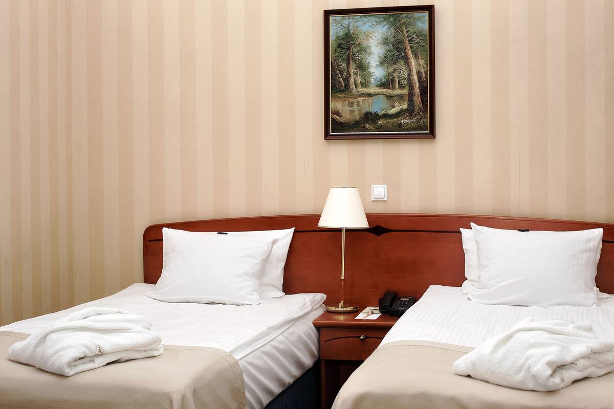 Ein Hotelzimmer mit zwei Betten, einem Nachttisch, einer Lampe und einem Gemälde an der Wand.