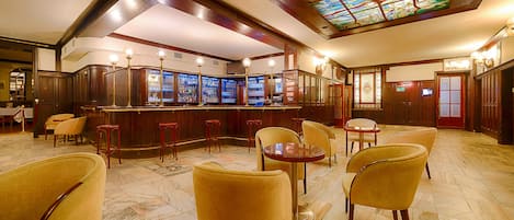 A bar area with multiple stools and tables, a stained glass ceiling, and a bar counter with a display case.