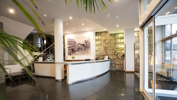 A modern lobby with a reception desk, a staircase, and a stone wall. - Legendary Porto Hotel (Porto)