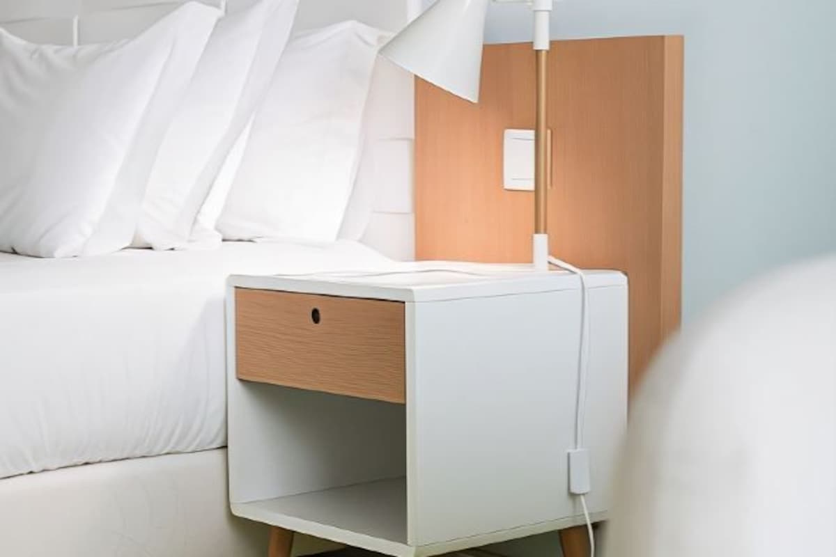 A white bedside table with a lamp, a drawer, and a power outlet.