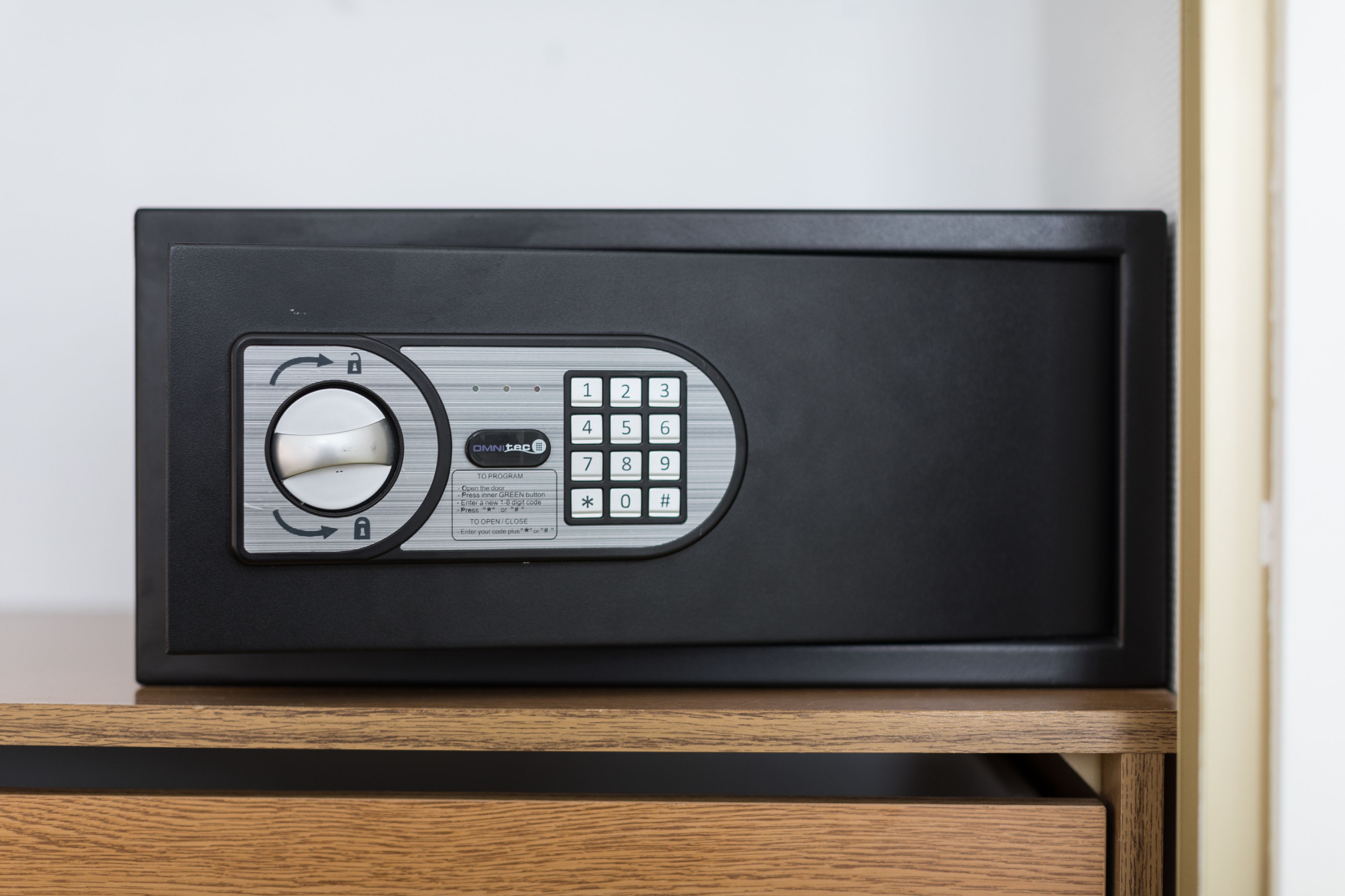 A black safe with a combination dial and keypad, placed on a wooden surface.