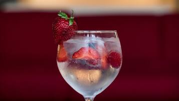 A cocktail glass with ice and strawberries on a reflective surface, with a blurred background of lights.