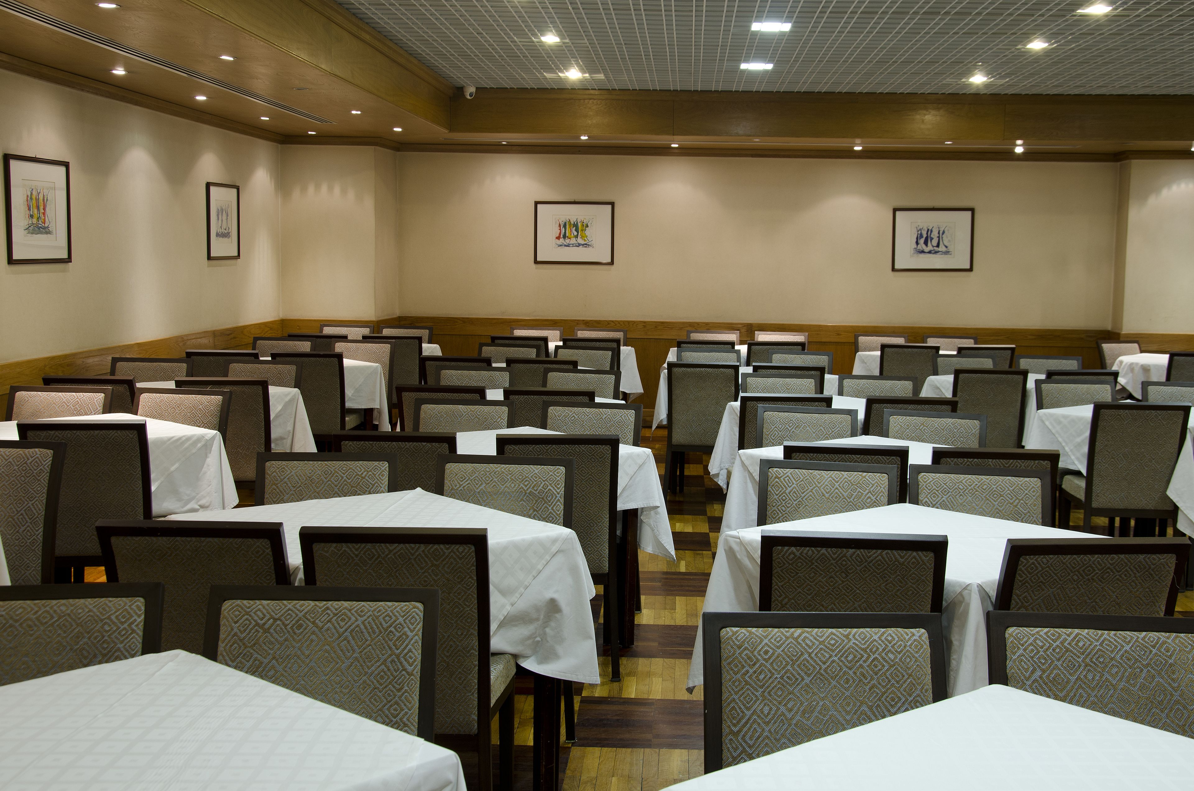 A conference room with rows of tables and chairs, framed artwork on the walls, and a wooden panel design on the lower half of the walls.