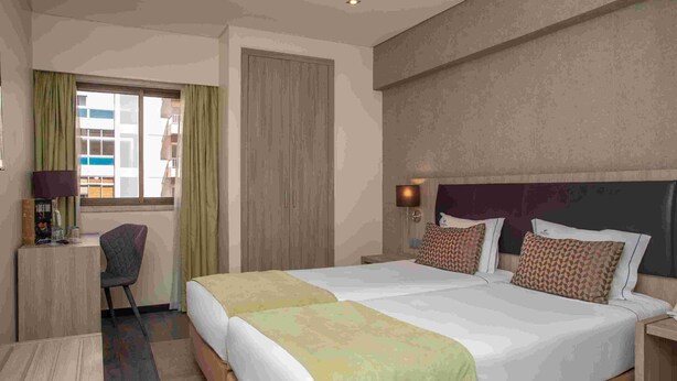 Une chambre d’hôtel avec un grand lit, un bureau, une chaise et une fenêtre avec des rideaux.