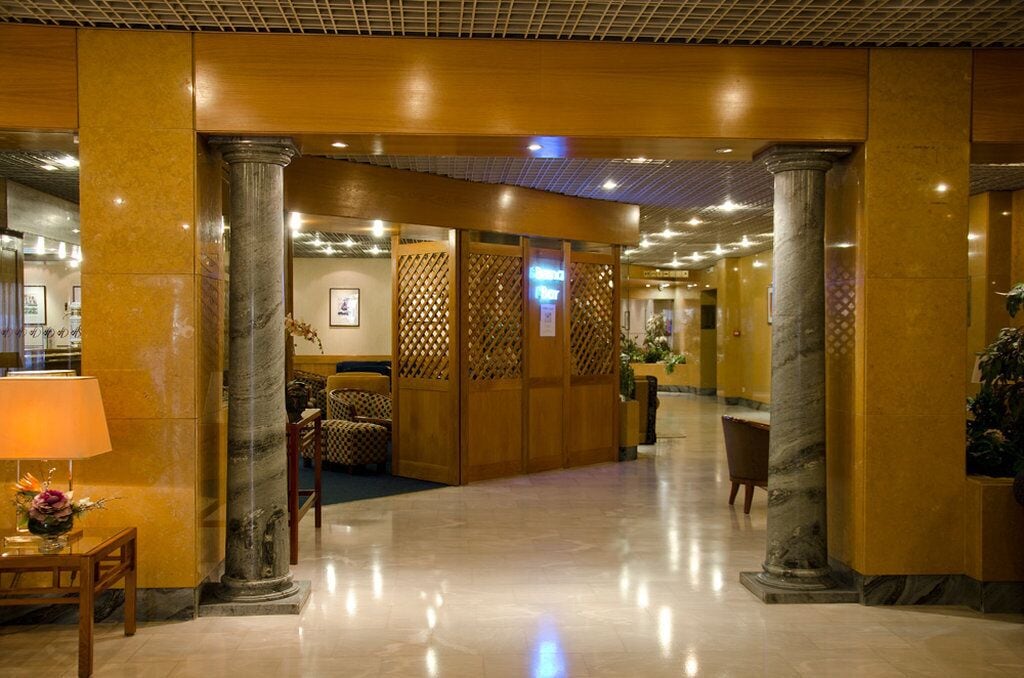 Un vestíbulo de hotel con suelo de mármol, columnas de madera y una mesa de recepción.
