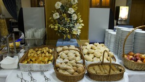 Une table de buffet proposant une variété de plats, notamment du pain, des pâtisseries et des fruits, ainsi qu’un centre de table floral.