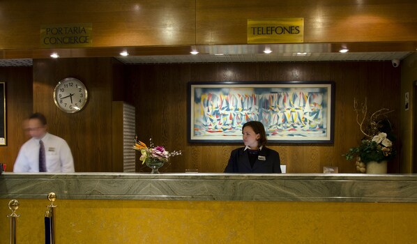 Un mostrador de recepción de hotel con un reloj, un letrero de teléfono y un cuadro.
