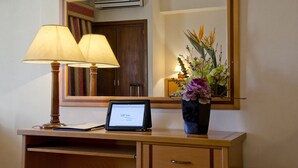 Un bureau avec un ordinateur portable, deux lampes, un vase de fleurs et un miroir qui reflète une porte et un appareil de climatisation.