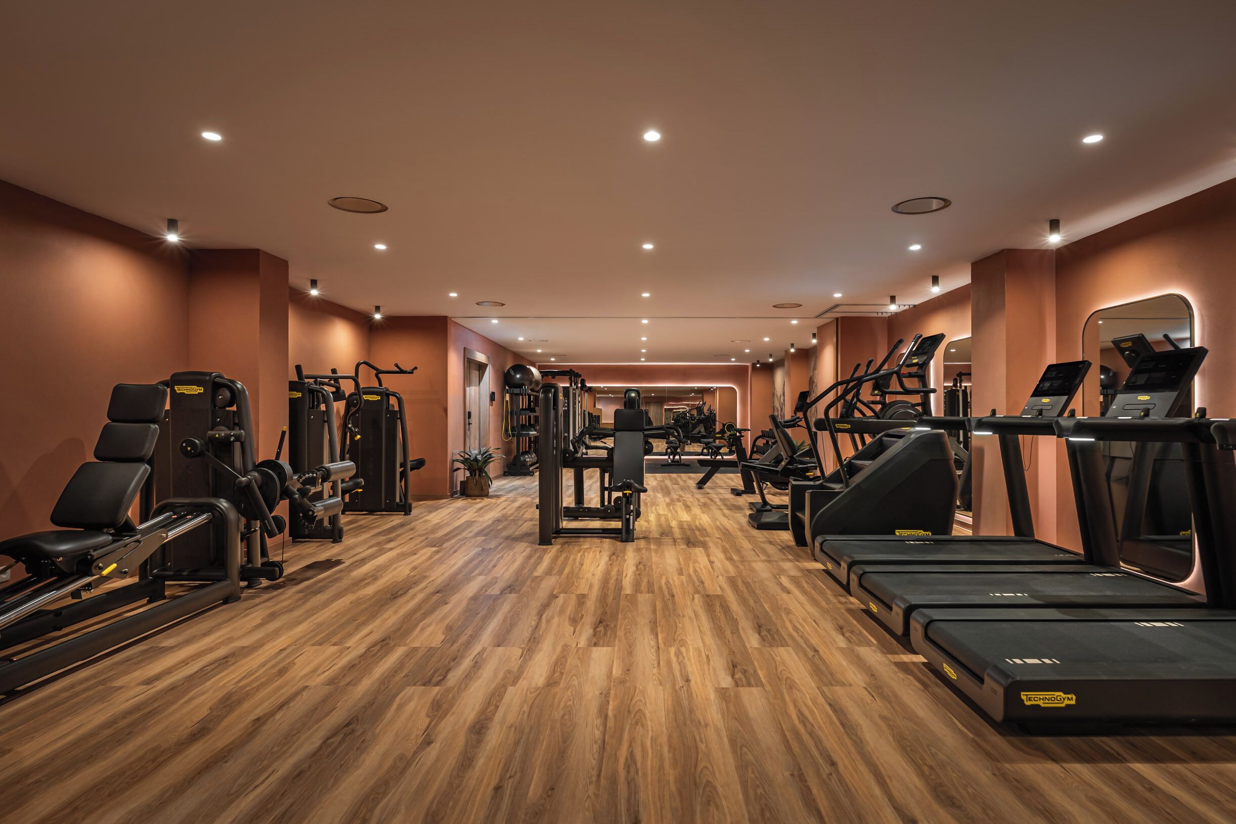 Een sportschool met cardio-apparaten, gewichten en een houten vloer.