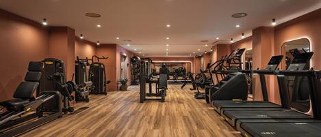 Un gimnasio con máquinas de cardio, equipo de levantamiento de pesas y piso de madera.