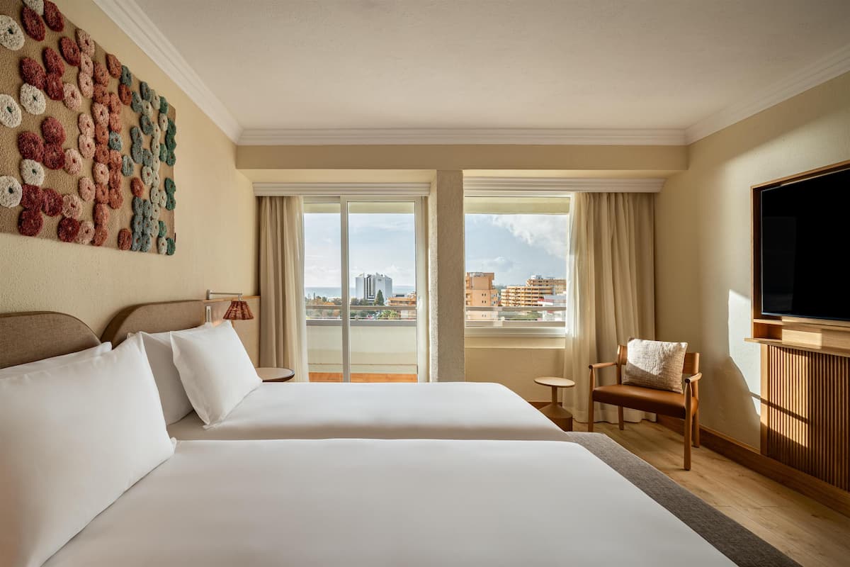 A hotel room with two beds, a large window, a television, and a wall art piece.