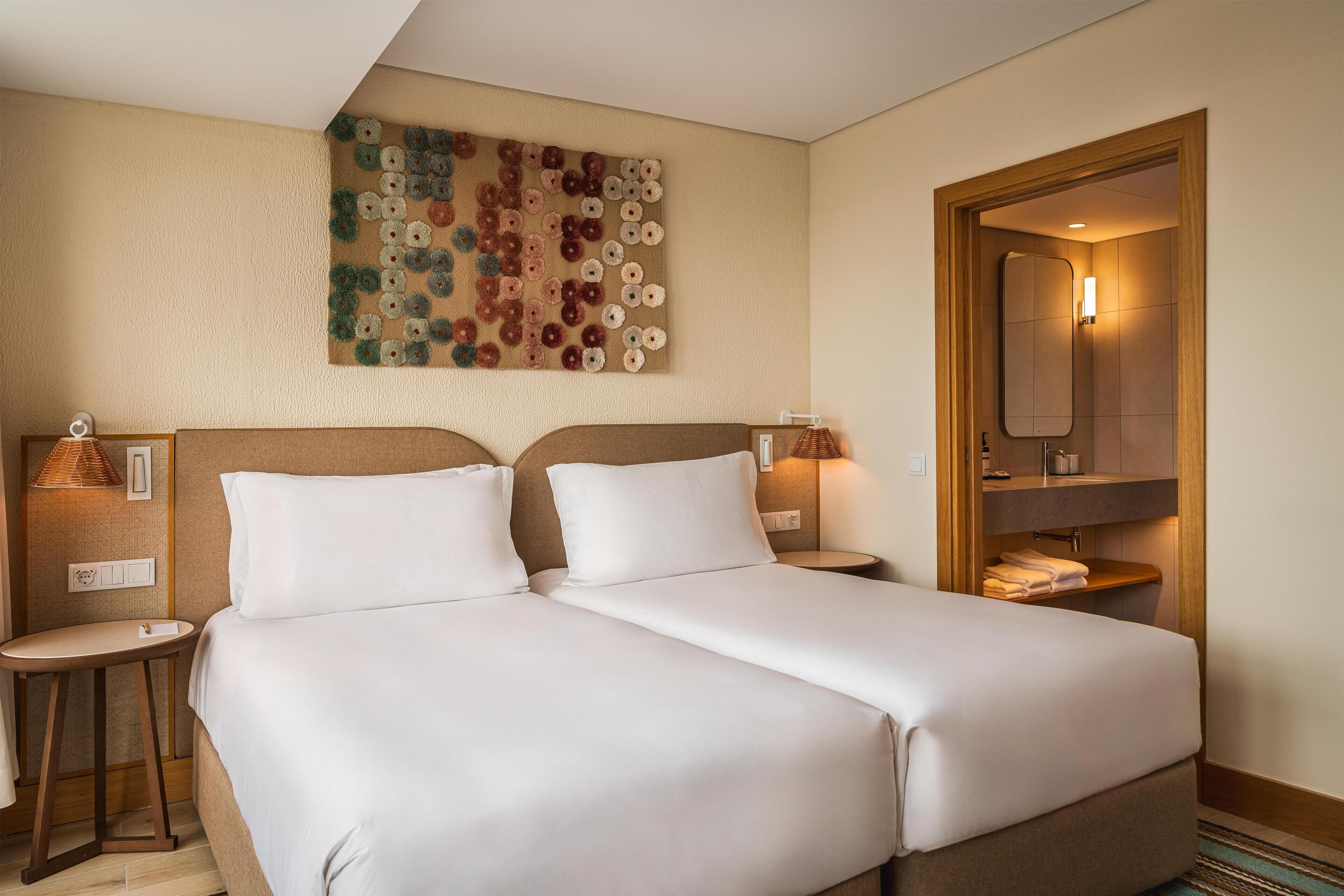 Une chambre d’hôtel avec deux lits, une œuvre d’art murale, un miroir et une petite table avec une lampe.