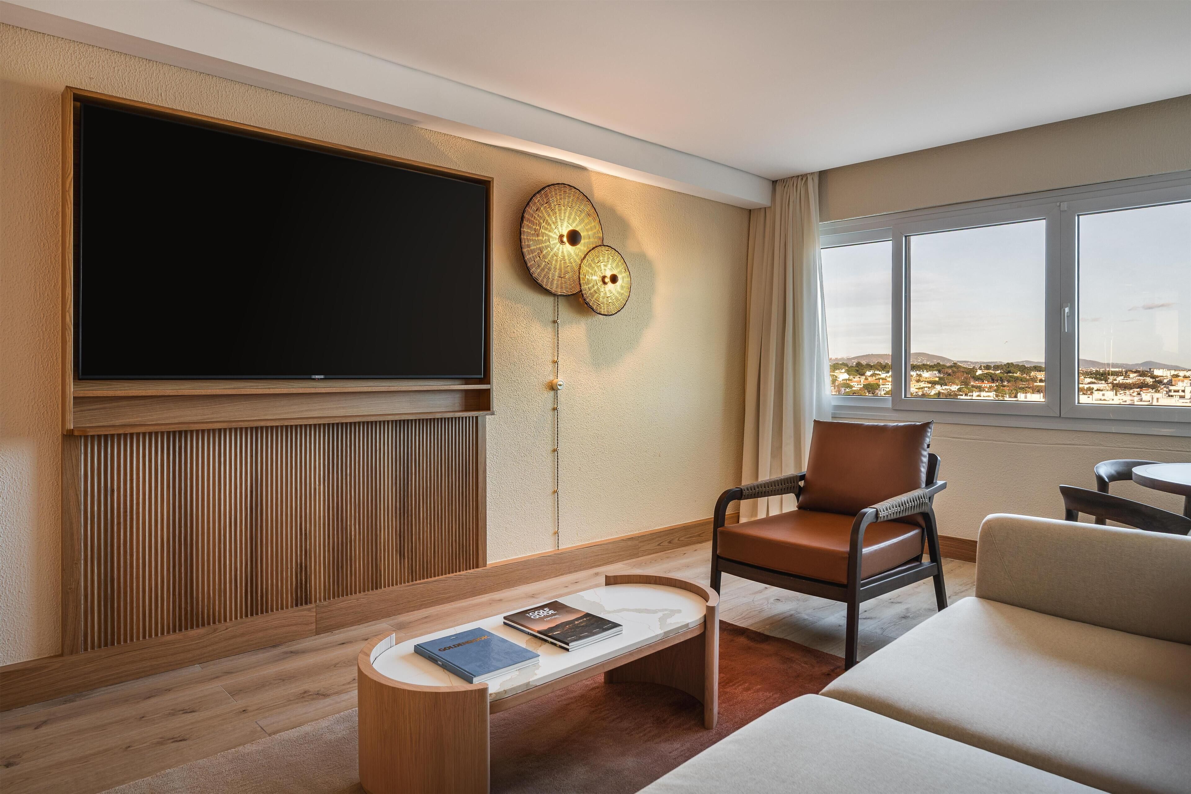 Un moderno salón con un televisor de pantalla plana grande, un banco de madera con libros, un sillón de cuero marrón y un sofá.