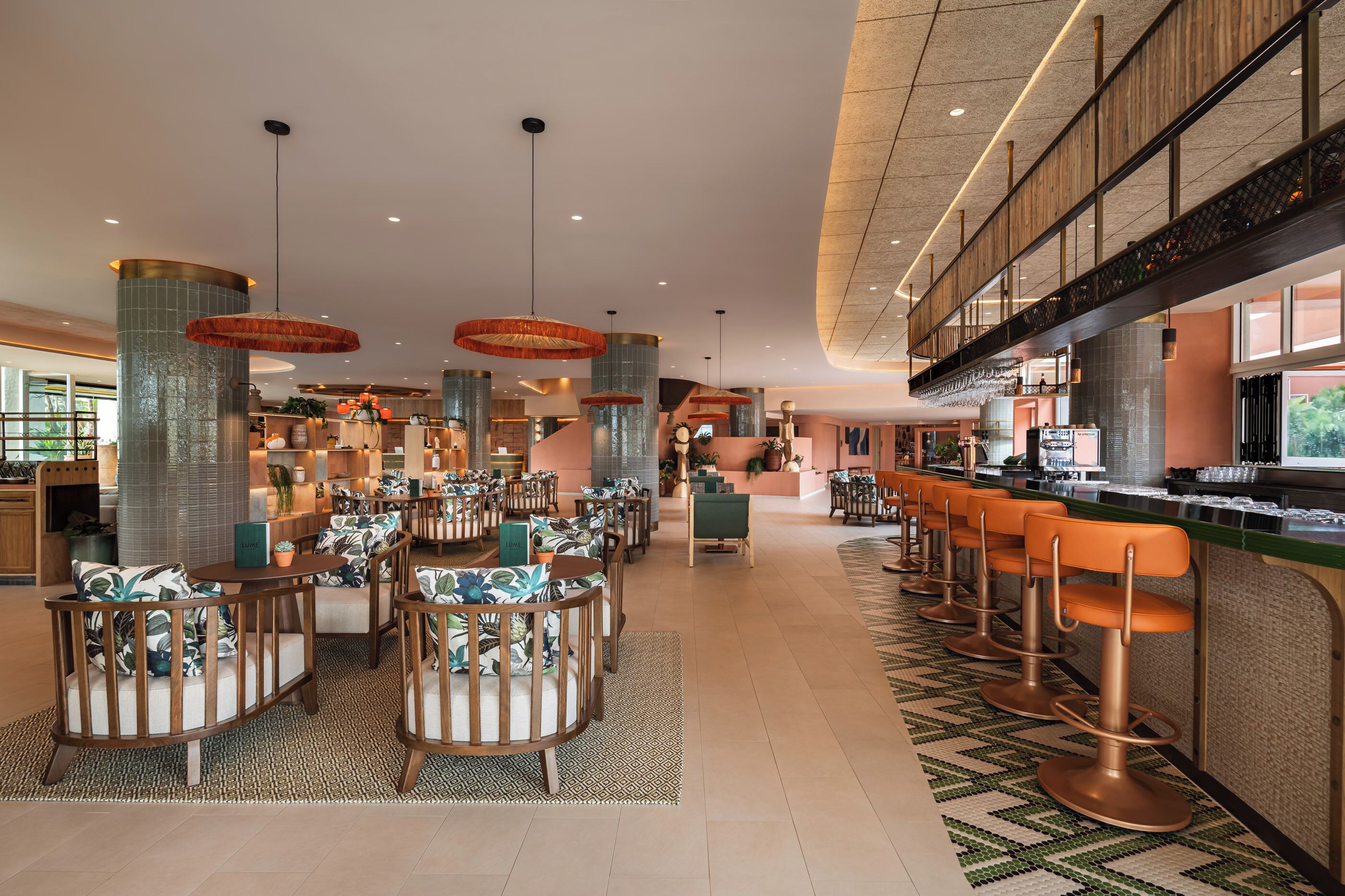 A spacious lobby with high ceilings, a central bar area with stools, and a staircase leading to an upper level.