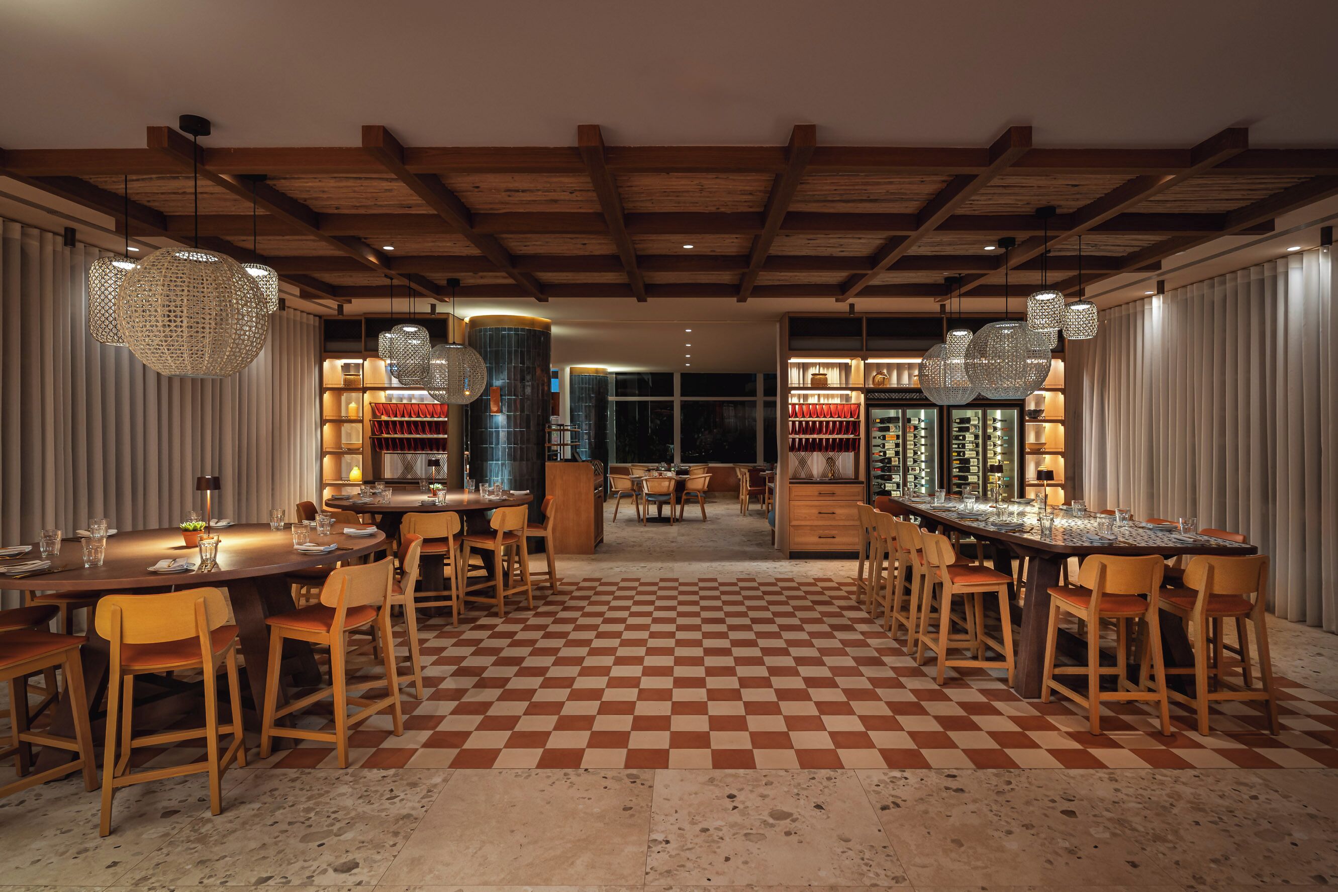 A restaurant with a checkered floor, wooden furniture, and hanging spherical light fixtures.