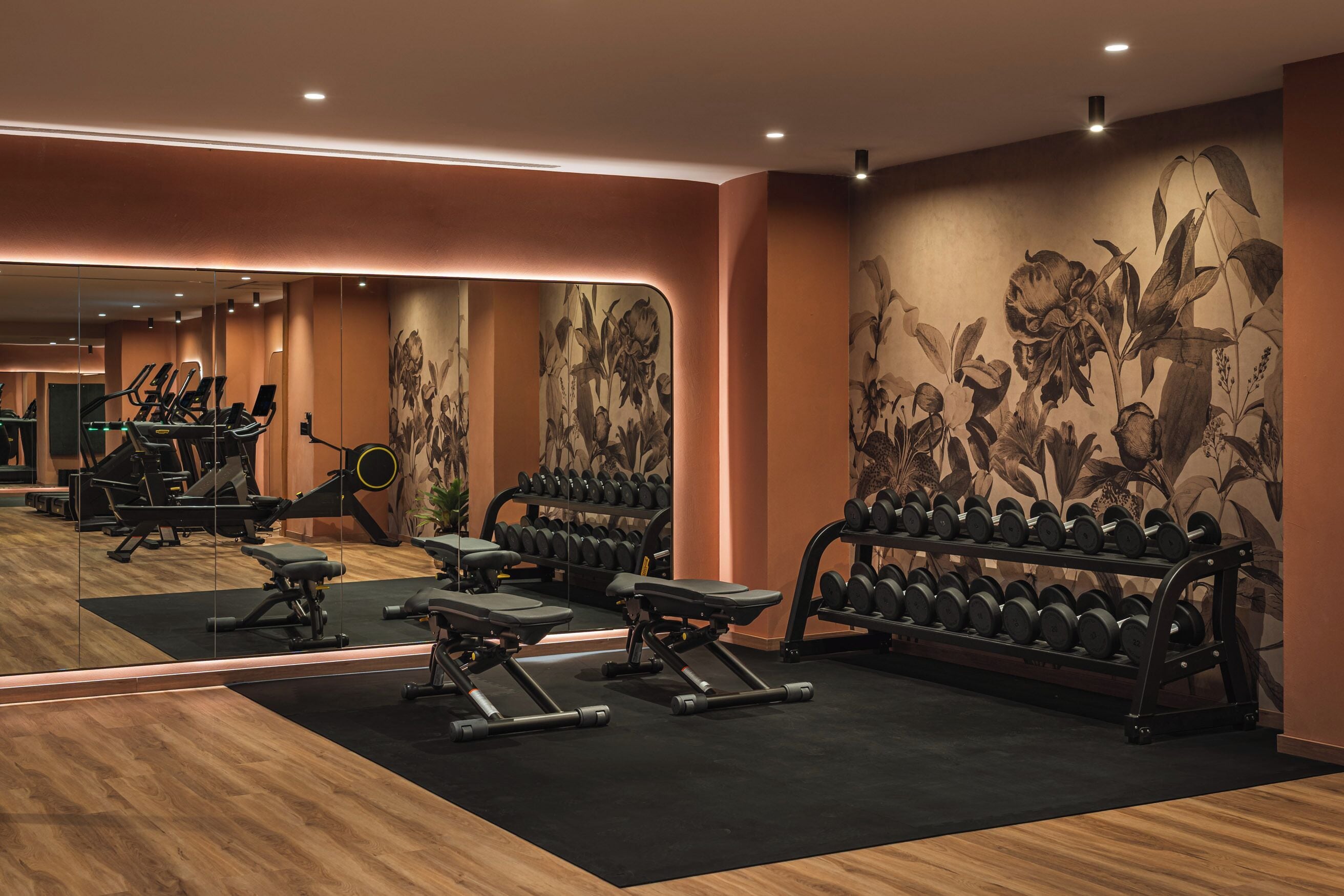 A gym with exercise equipment, mirrors, and a wall with a floral mural.