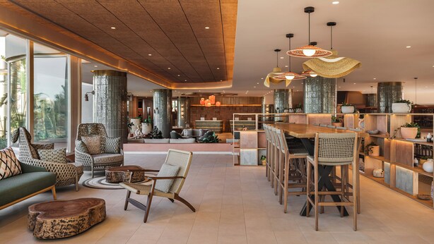 A spacious living area with a large sofa, a coffee table, and a dining area with bar stools. There are large windows providing natural light and a view of the outdoors. - Hyatt Regency Vilamoura Algarve (Loule)