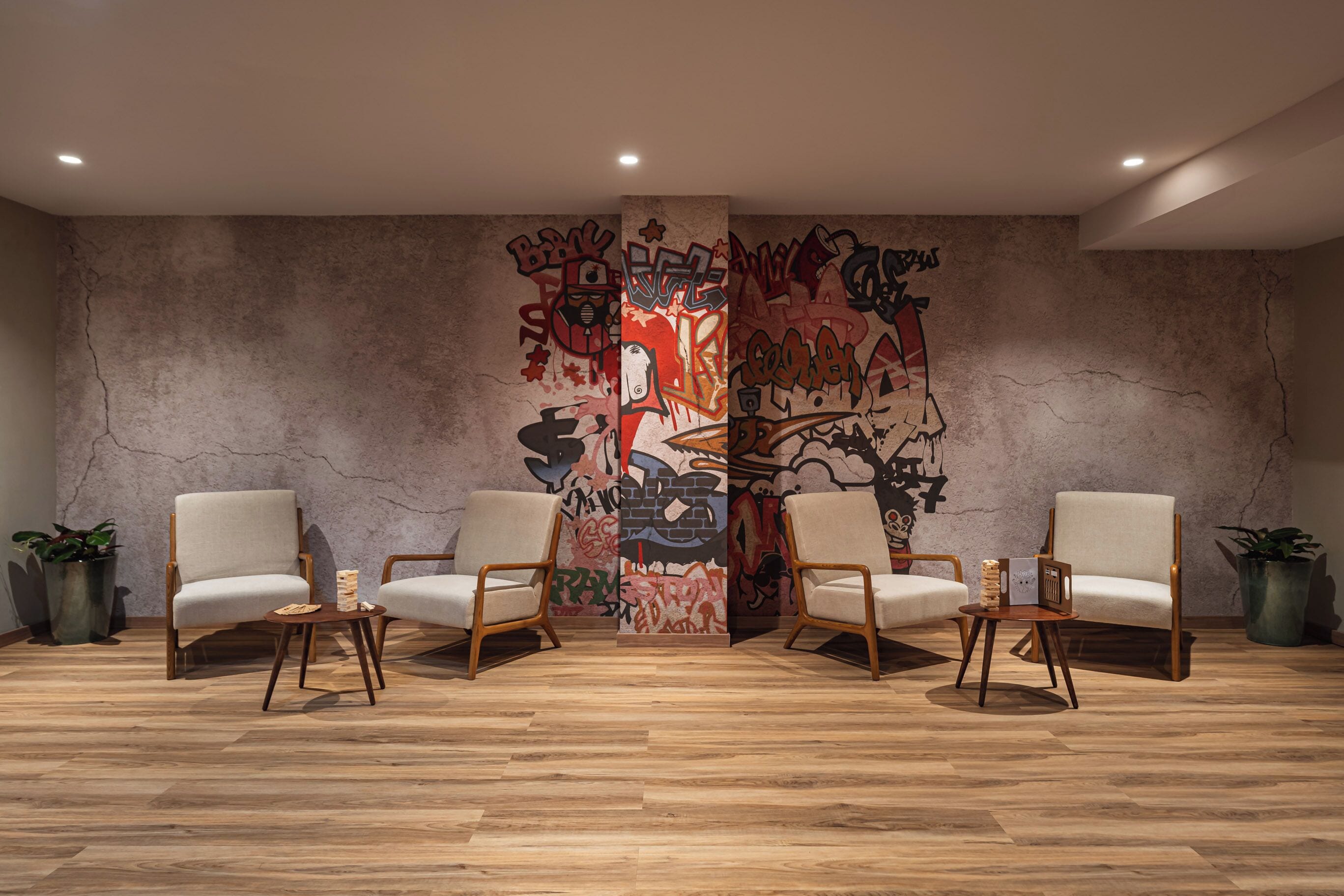 A room with a large graffiti wall, two white armchairs, a small wooden table, and potted plants.